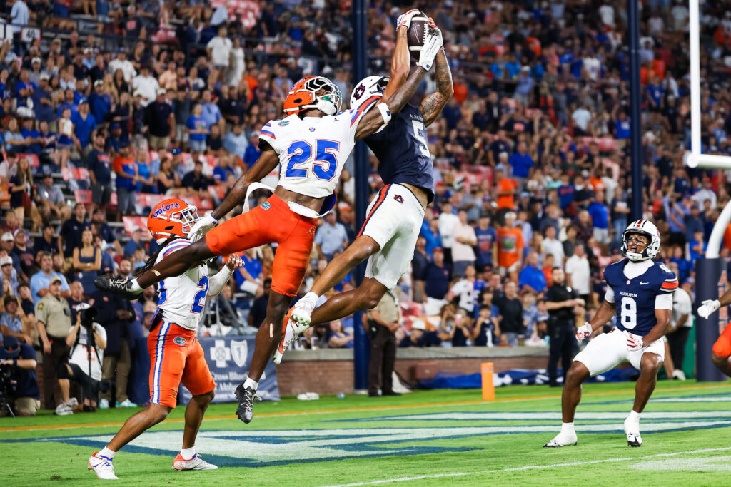 Two football players leap in mid-air to compete for a catch during a game, with one player securing the ball while another attempts to defend.